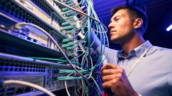 Focused serious experienced data center IT technician doing performance checking of twisted-pair cables