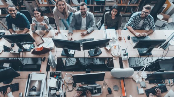 Young and successful. Top view of group of young business people in smart casual wear working together and smiling while sitting at the large office desk