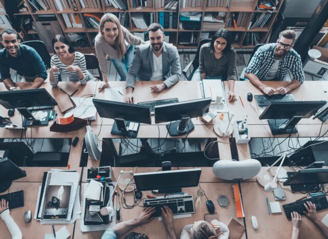 Young and successful. Top view of group of young business people in smart casual wear working together and smiling while sitting at the large office desk